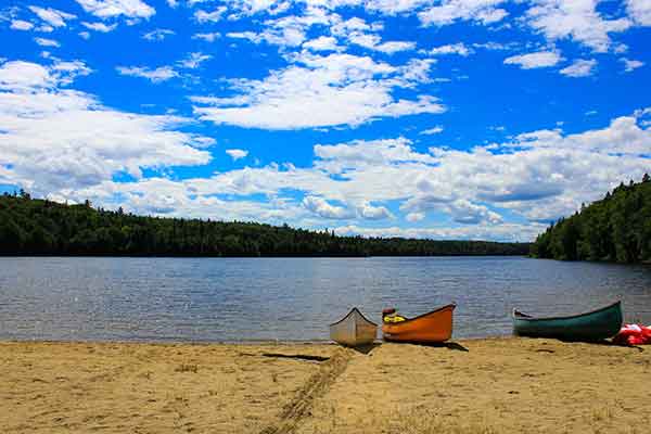 photo of canoes lined up along a swimming beach from boost your camping skills with these smart ideas